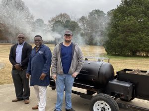 dean, instructor, and student posing in front of grill