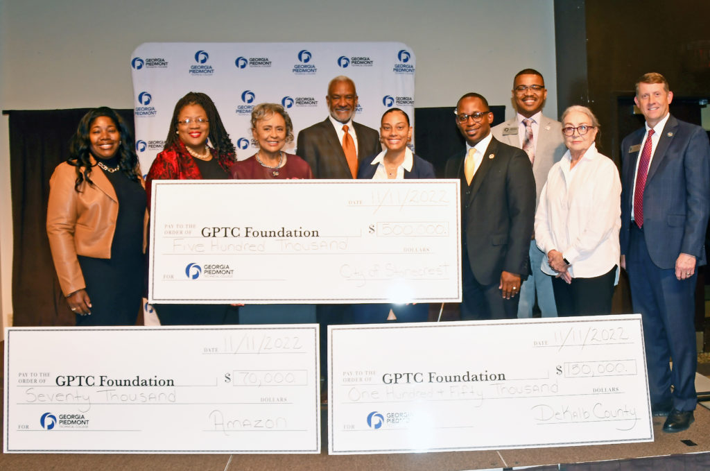 Officials from GPTC, TCSG, City of Stonecrest, Amazon and DeKalb County Commissioners pose with three giant checks totaling $720,000