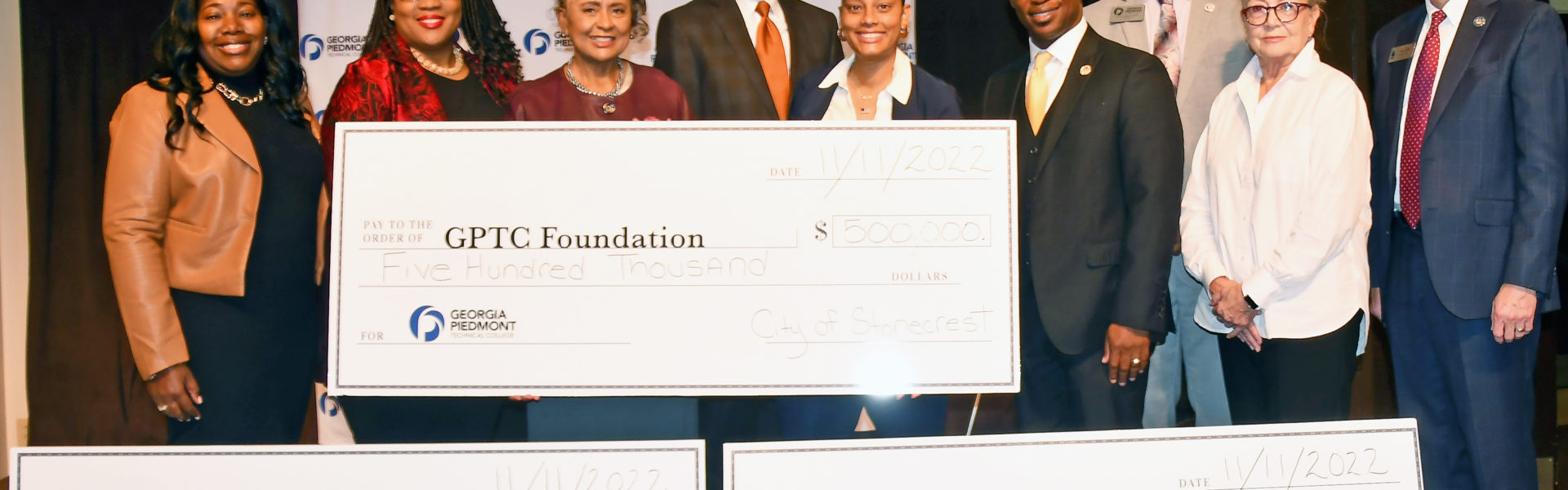 Officials from GPTC, TCSG, City of Stonecrest, Amazon and DeKalb County Commissioners pose with three giant checks totaling $720,000