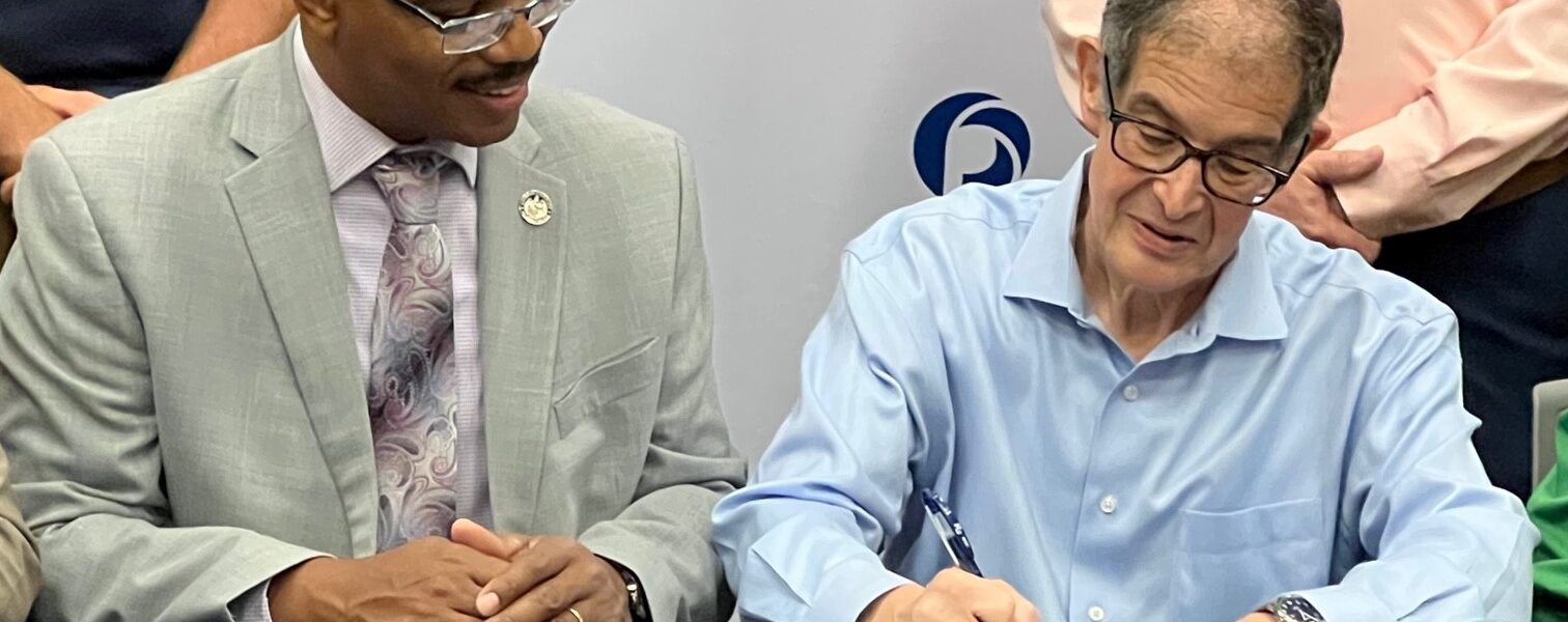 President Holston looks on as Government & Public Affairs Manager for Radius Recycling signs the paperwork.